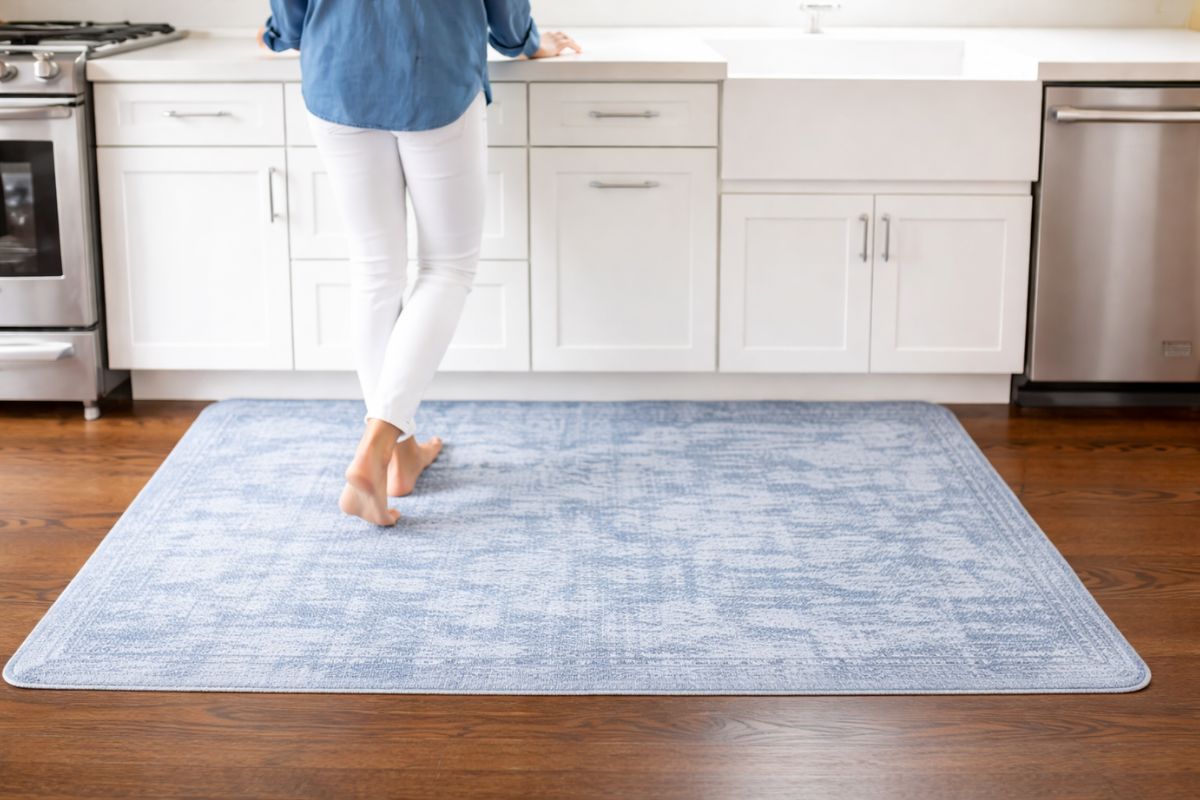 Osoba stoji bosa na plavom tepihu postavljenom ispred kuhinjskih elemenata u svetloj, modernoj kuhinji